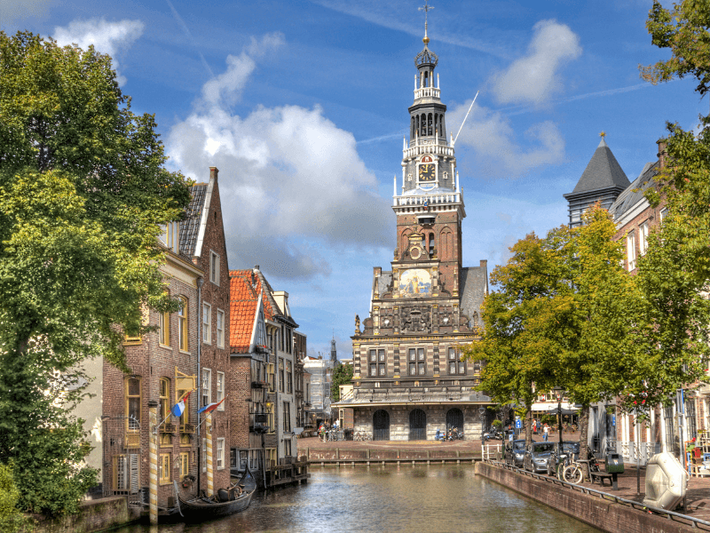 Historisch stadsbeeld van Alkmaar met de grachten en de iconische Waagtoren onder een blauwe lucht.